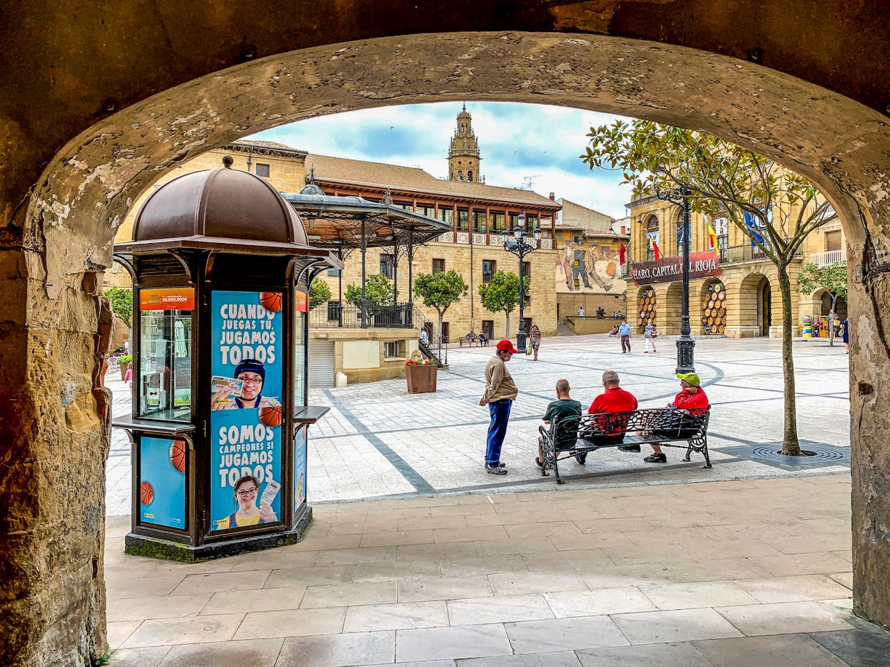 Charming view of a plaza in Haro, La Rioja, showing local architecture and people enjoying a sunny day.
